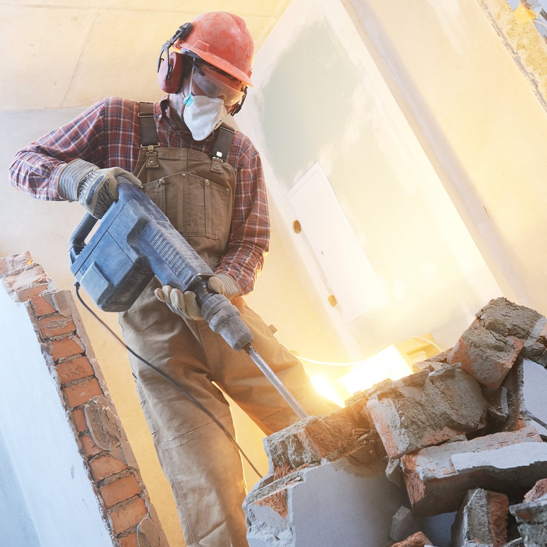 man working with a hand tool with hardhat, mask and ear protection on.