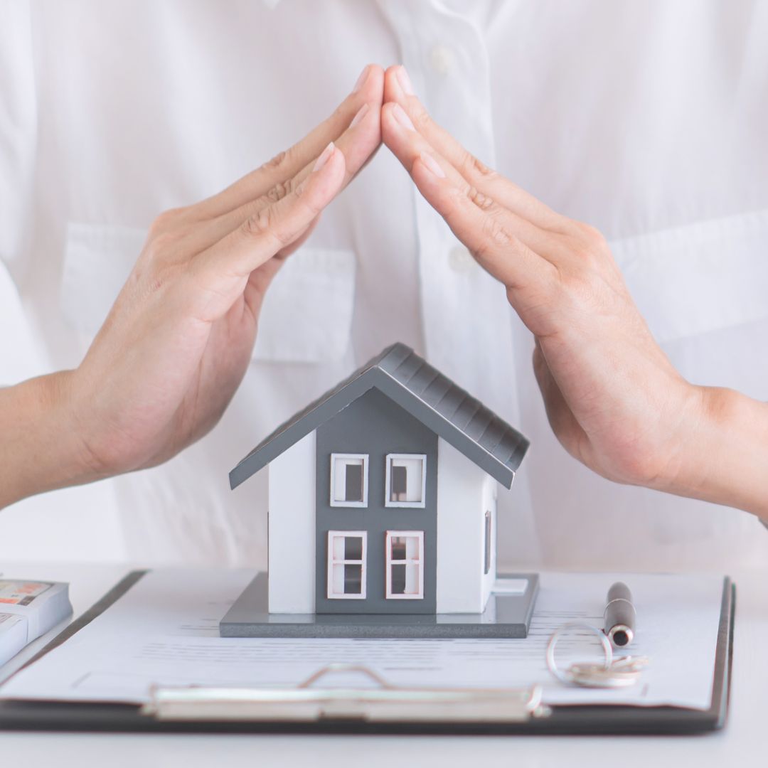 Person with their hands covering a model home in protection.